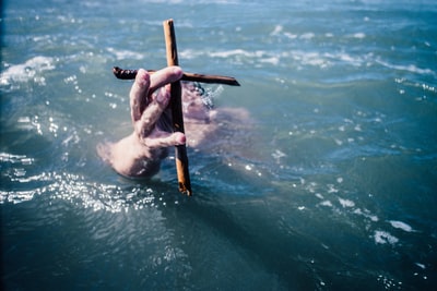 人在水上面拿着棕色的木十字架在白天
